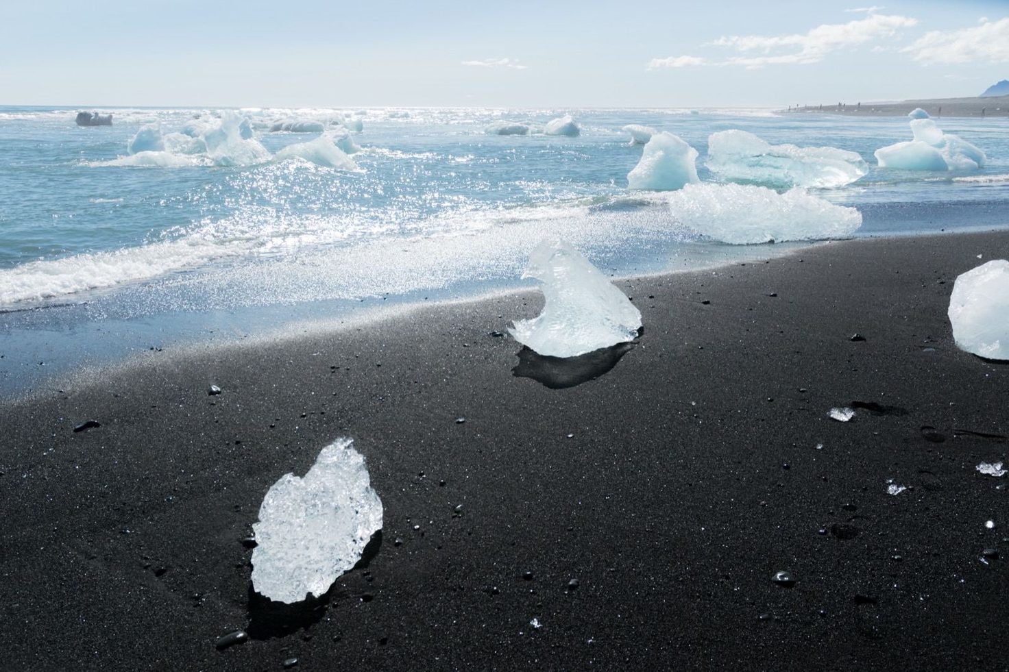 Chunks of glacial ice scattered on a black sand beach at the water's edge