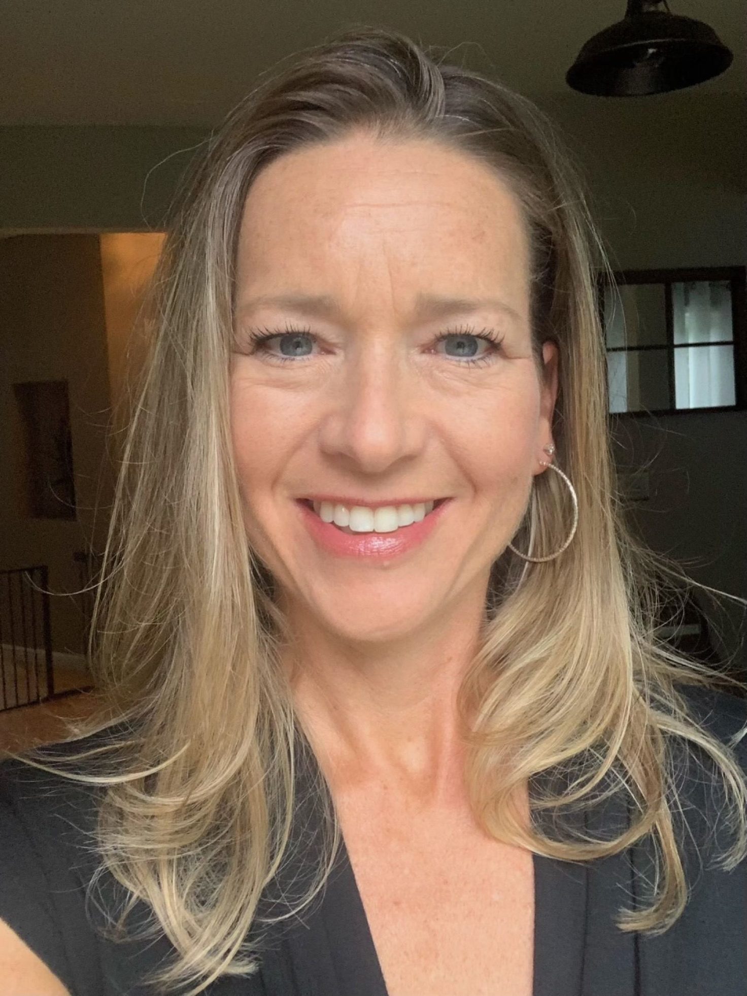 A smiling woman with long blonde hair and hoop earrings