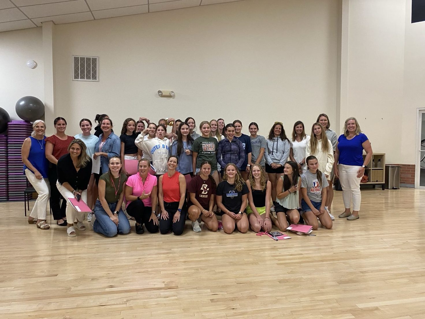 A large group of women and teen girls pose together in a fitness studio