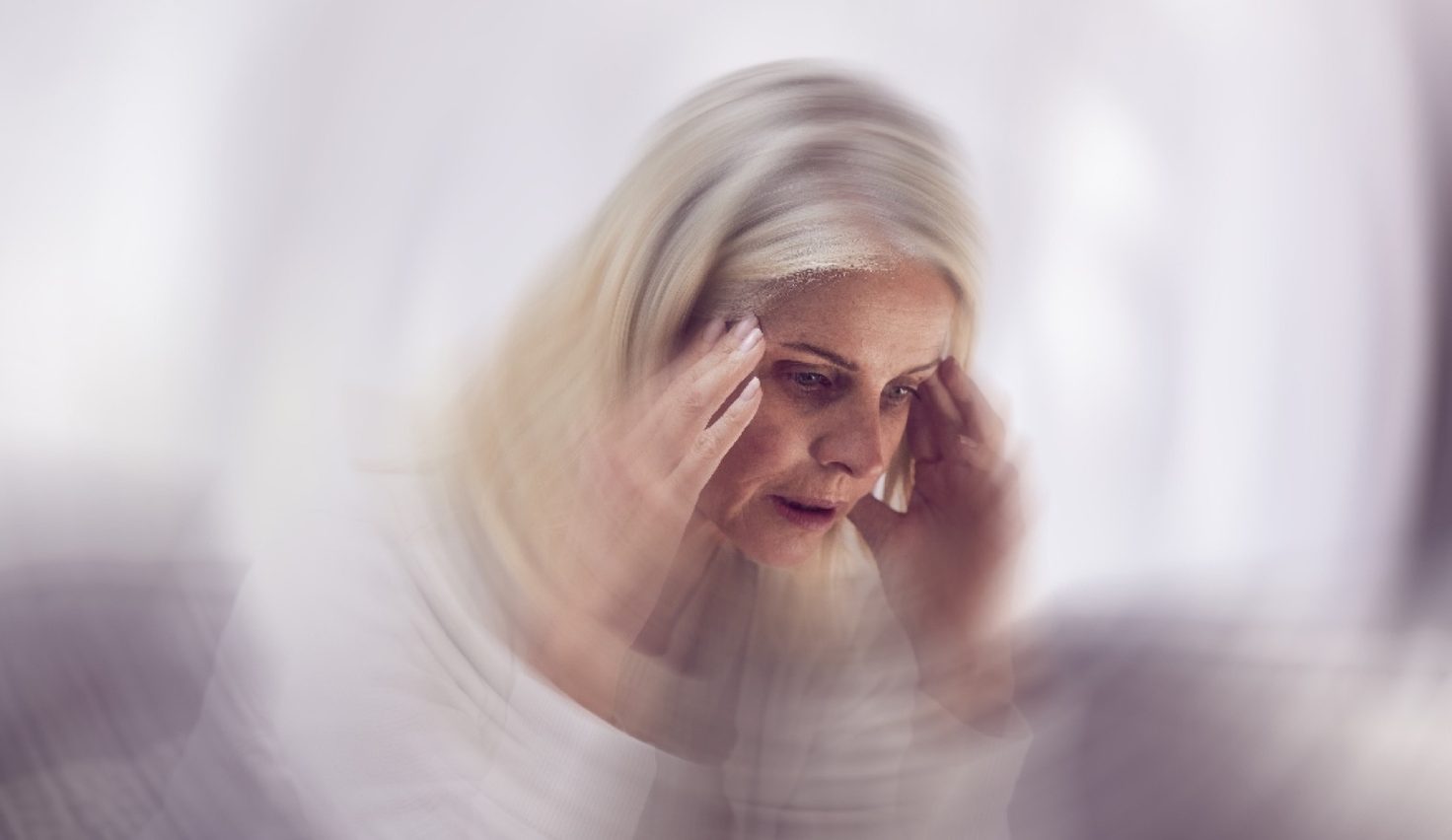 Motion-blurred photo of an older woman holding both hands to her temples
