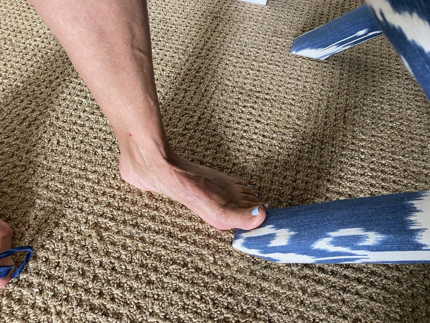 Close-up of a bare foot standing on carpet beside a blue patterned chair leg